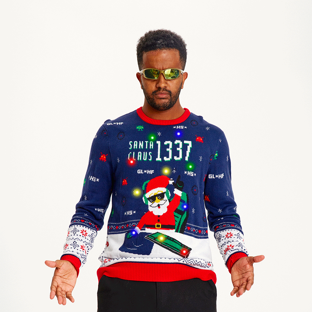 Un homme posant portant un pull de Noël bleu et rouge avec un Père Noël et des lumières.
